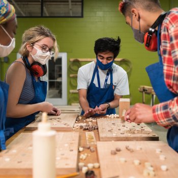 group of students wearing masks working on a wood projects aroumnd a table in a workshop