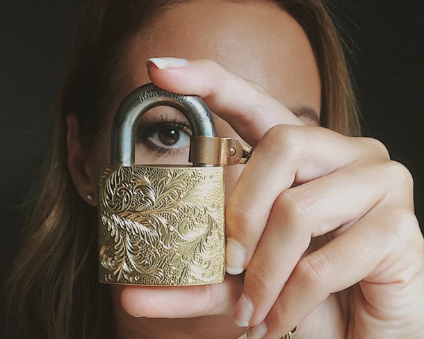 Self-portrait of a person holding up an ornately engraved lock with one eye visible through the loop