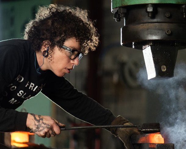blacksmith working a bar of glowing metal in her studio