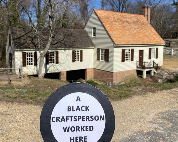 historic house with sign being held up in foreground that says a black craftsperson worked here