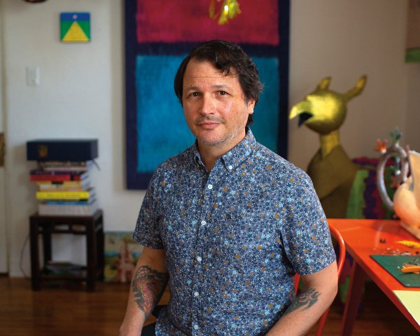 Roberto Benavidez in his studio surrounded by completed works, including Sugar Skull Piñata No.1, 2009, his very first piñata sculpture, which hangs just below the tail of one of his Bosch birds. Photo by James Bernal.